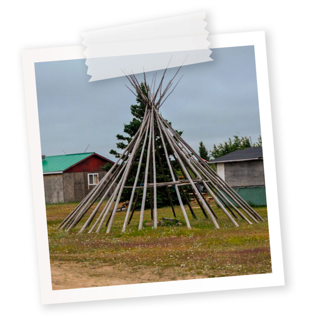 A polaroid of a teepee on Fort George island that has abandoned cabins in the background.